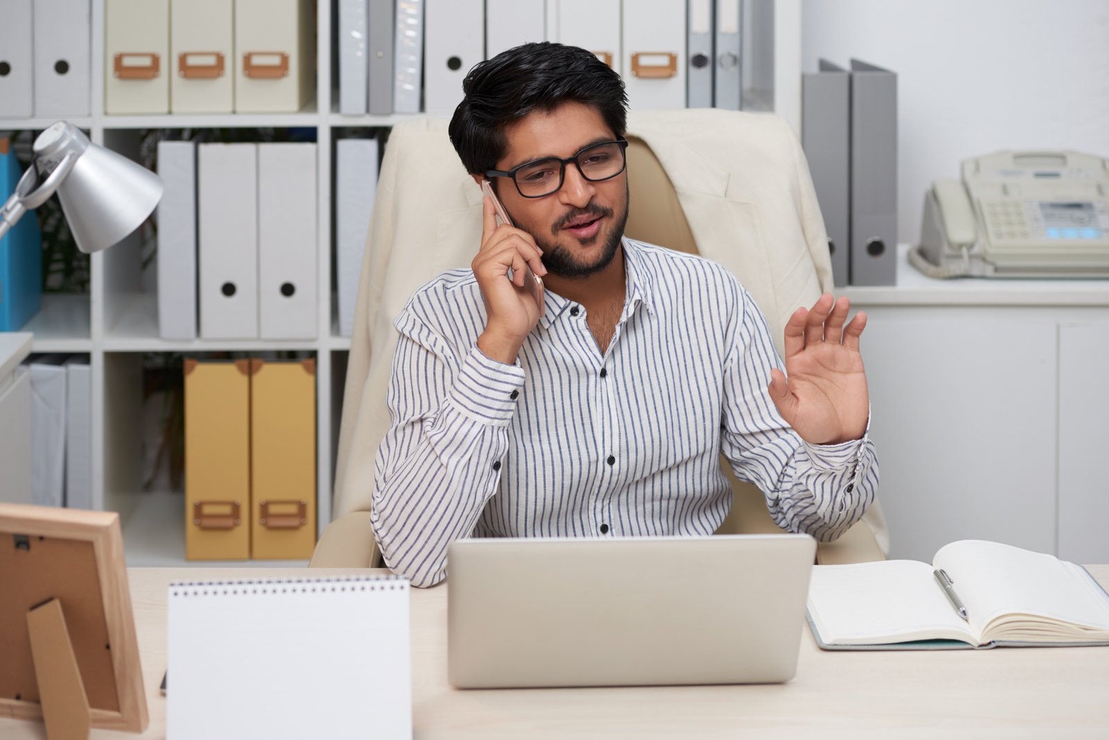 Cheerful Indian businessman talking on phone with colleague