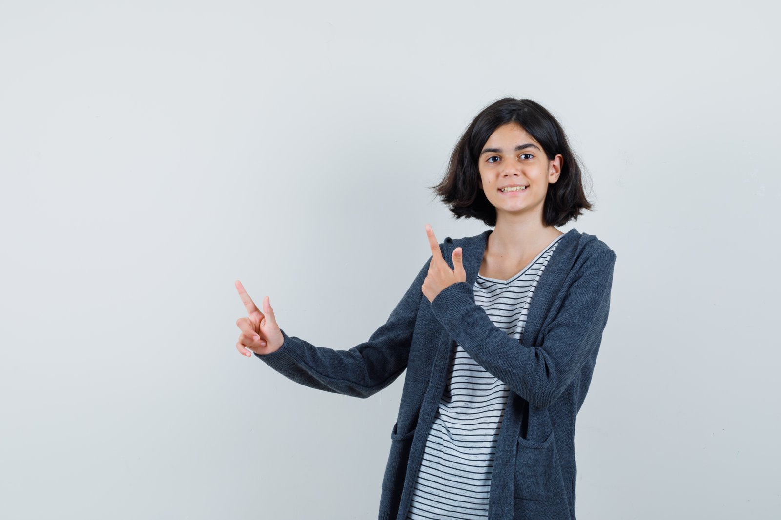 Little girl in t-shirt, jacket pointing at upper left corner and looking cheerful , front view.